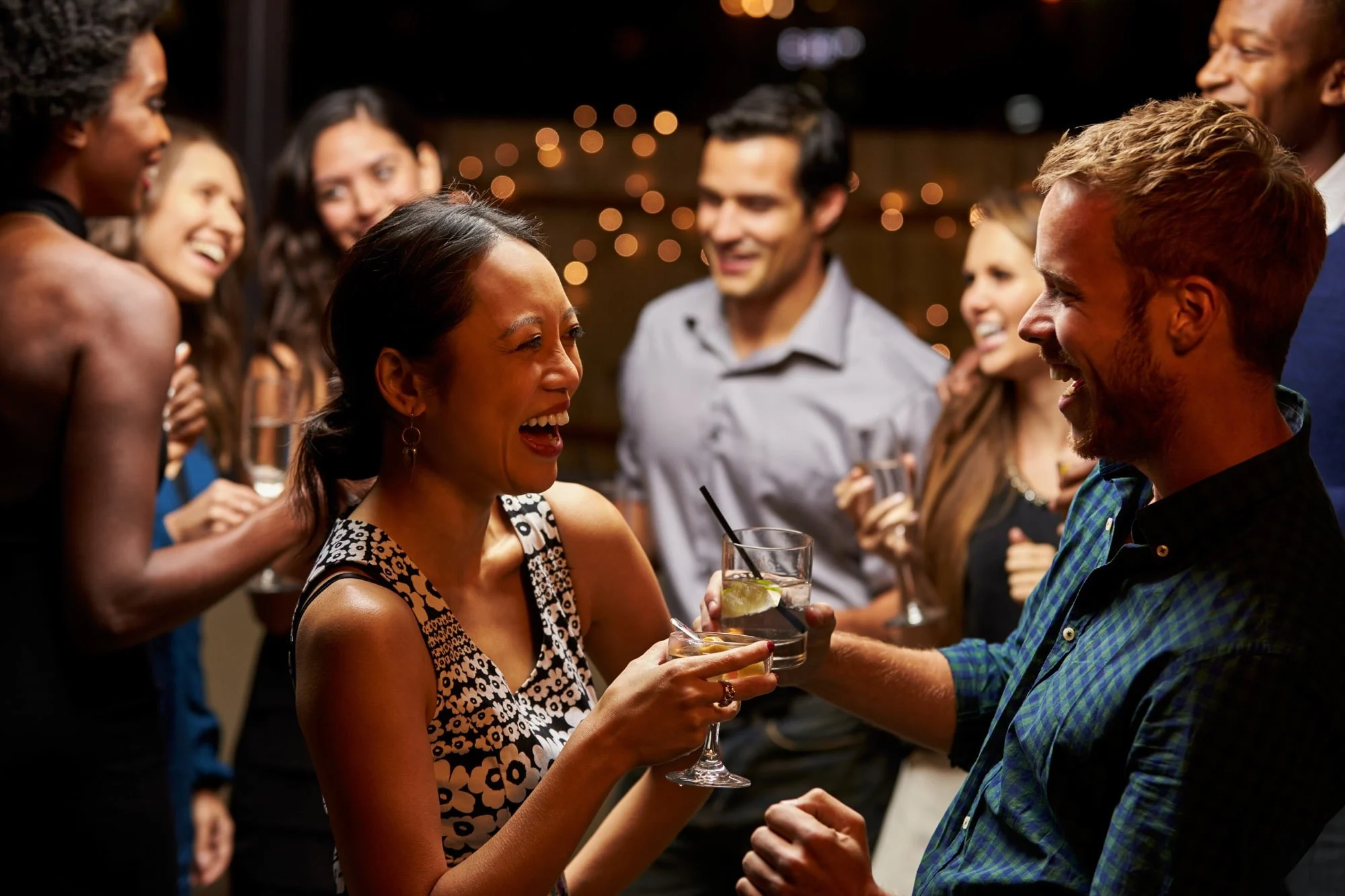 Two people in focus having a drink and a circle of happy people in the background